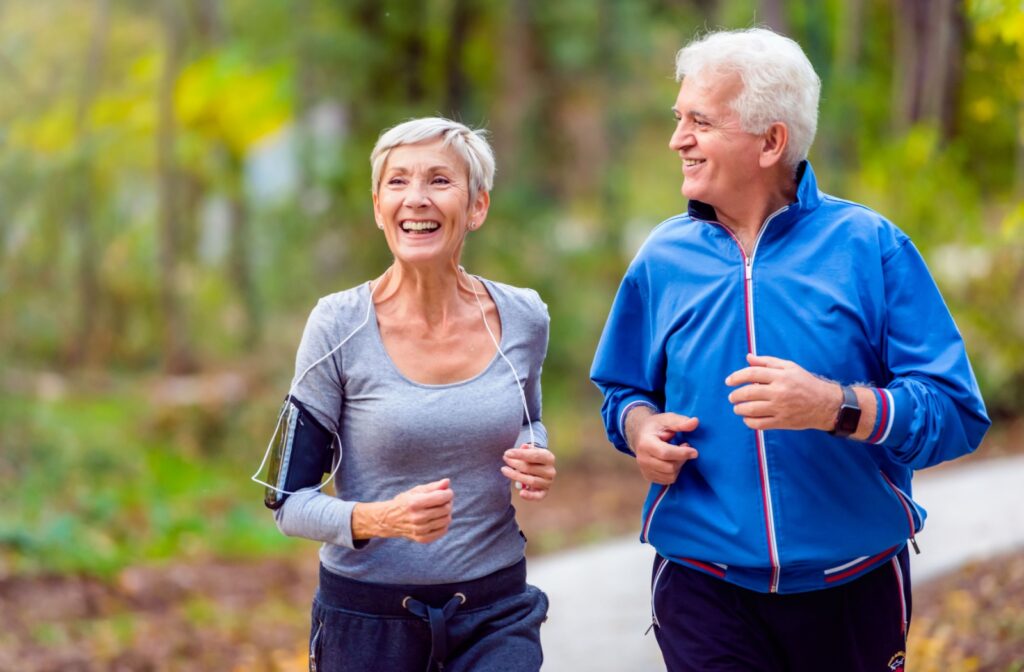 An older man and woman smiling while jogging outdoors.