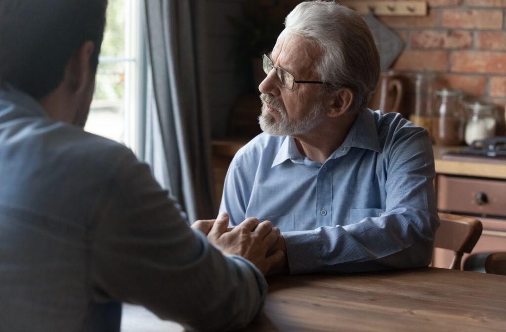 A man holds his senior father's hand as they discuss moving to memory care.