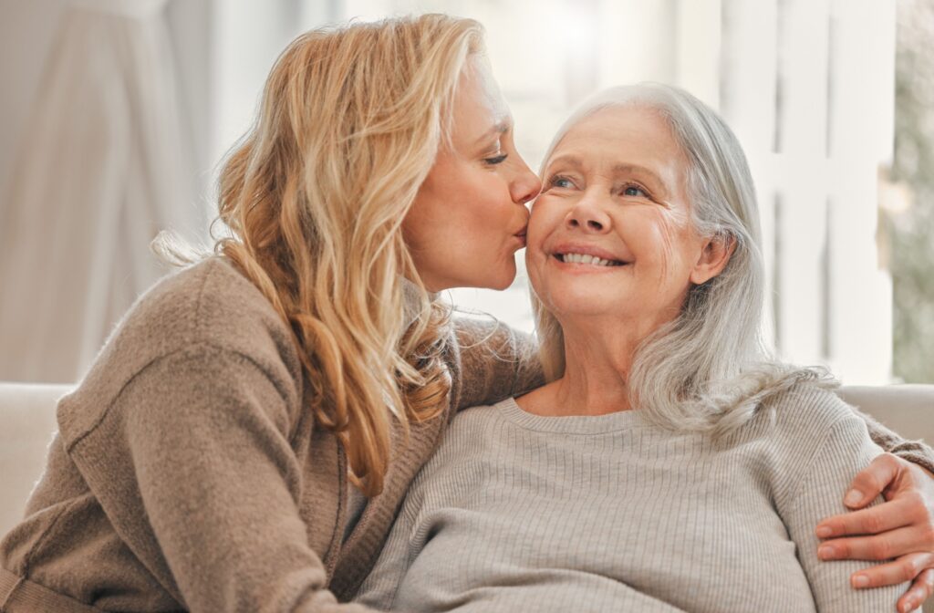 An adult child kissing their older parent's cheek during a visit in memory care.